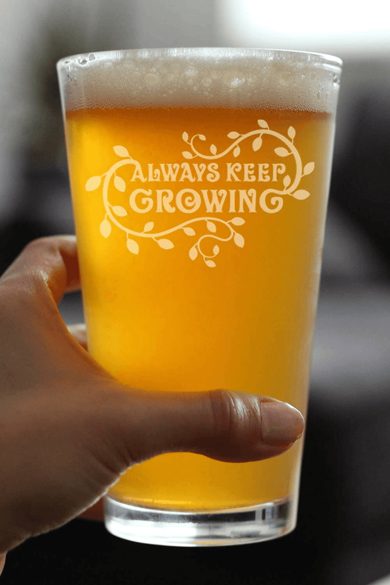 Handheld pint beer glass with 'Always Keep Growing' etched design, amber beer