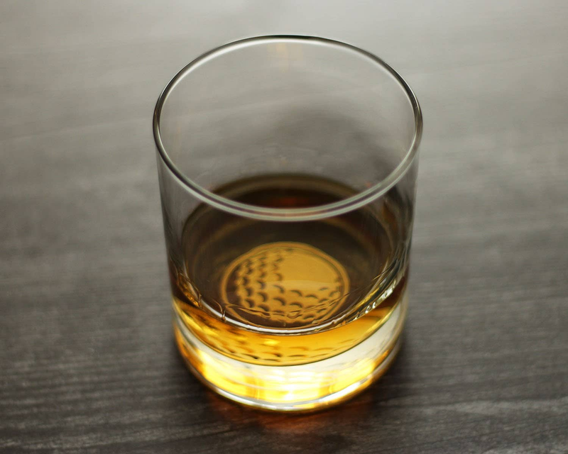 Whiskey rocks glass, front view, with golf-ball emblem on base and amber liquid