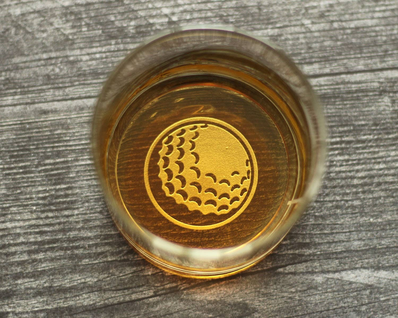 Golf-ball whiskey rocks glass, top-down, showing gold emblem on base with amber liquid