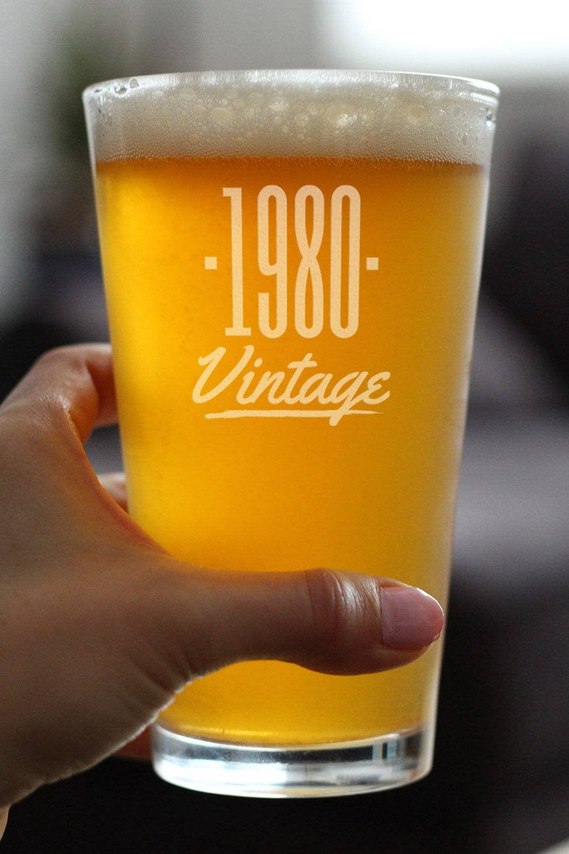 Hand holding 1980 Vintage pint glass filled with amber beer, foam top, etched -1980-