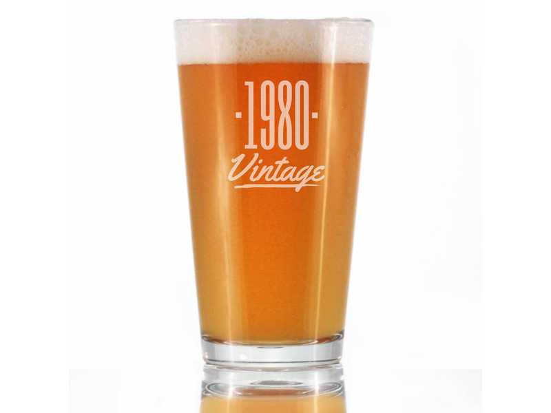 1980 Vintage etched pint glass filled with amber beer, clear rim, front view