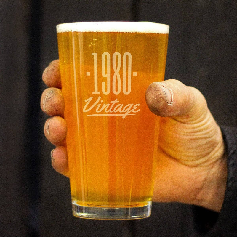 Person holding 1980 Vintage pint glass with amber beer, etched -1980- design, foam head