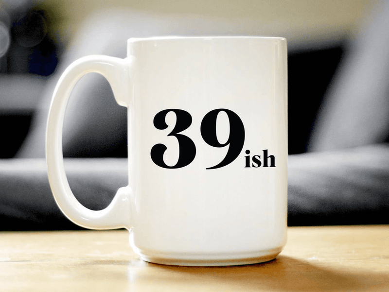 White ceramic coffee mug with black '39 ish' text, curved side view on tabletop