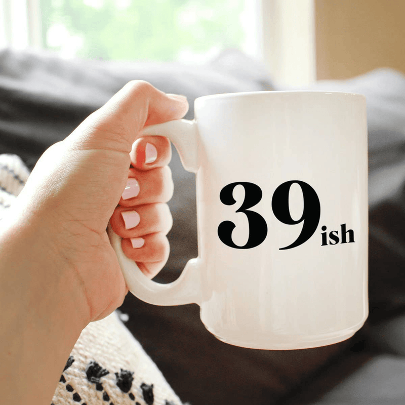 White ceramic coffee mug with black '39 ish' text, held by a hand