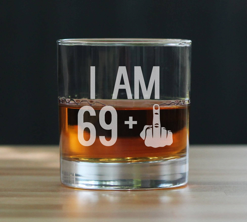 Whiskey rocks glass with “I AM 69+” middle finger etching and amber drink inside.