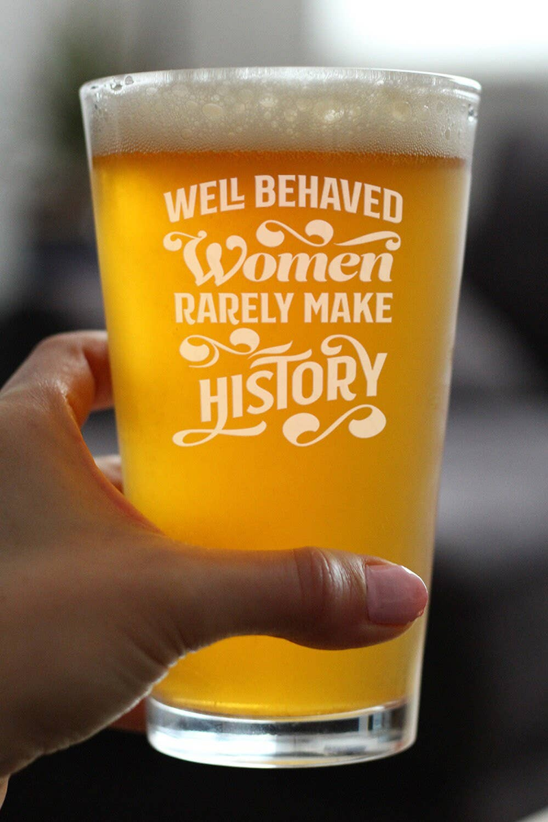 Hand holding beer pint glass with etched feminist slogan, amber beer with foam