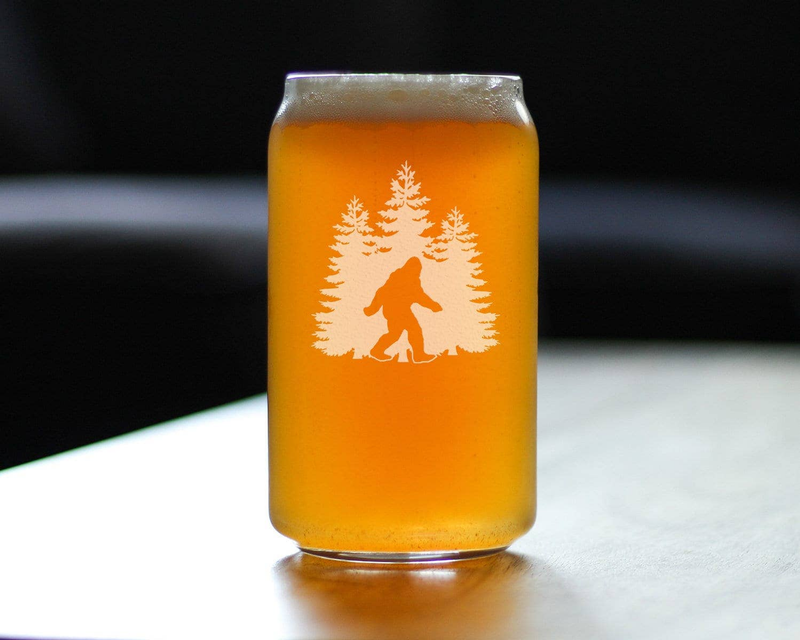 Pint beer can glass filled with amber beer and etched Sasquatch with pine tree design