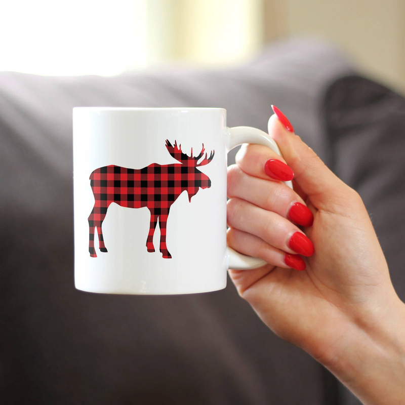 White coffee mug with red plaid moose silhouette, held with red nails