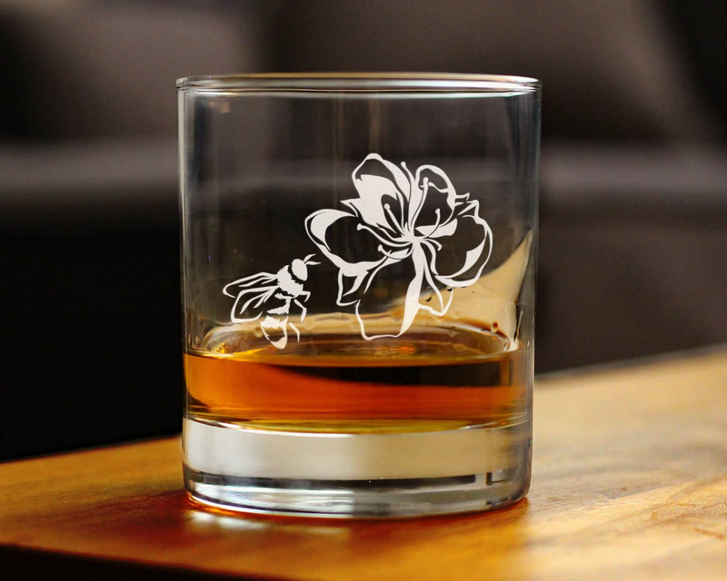 Clear whiskey rocks glass with etched flower and bee design, filled with amber liquid
