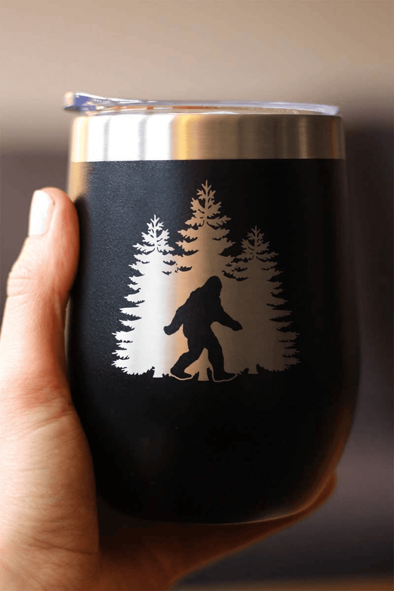 Black insulated wine tumbler with Bigfoot pine tree design, held in a hand
