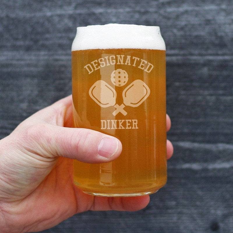 Hand holding amber beer can glass with etched Designated Dinker pickleball logo