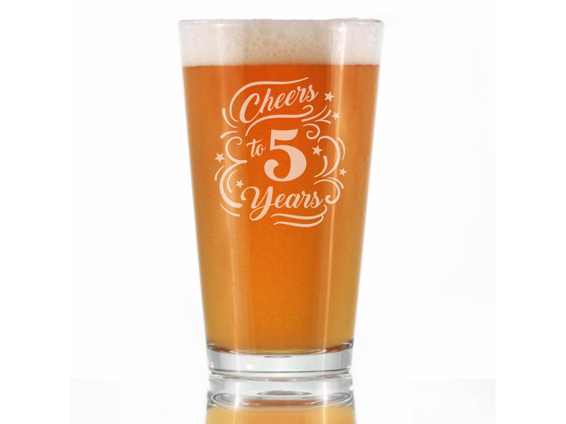 Front view of clear pint glass with amber beer foam, Cheers to 5 Years etched