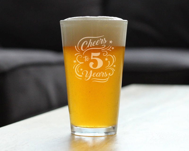 Clear pint glass filled with amber beer, Cheers to 5 Years etched on front