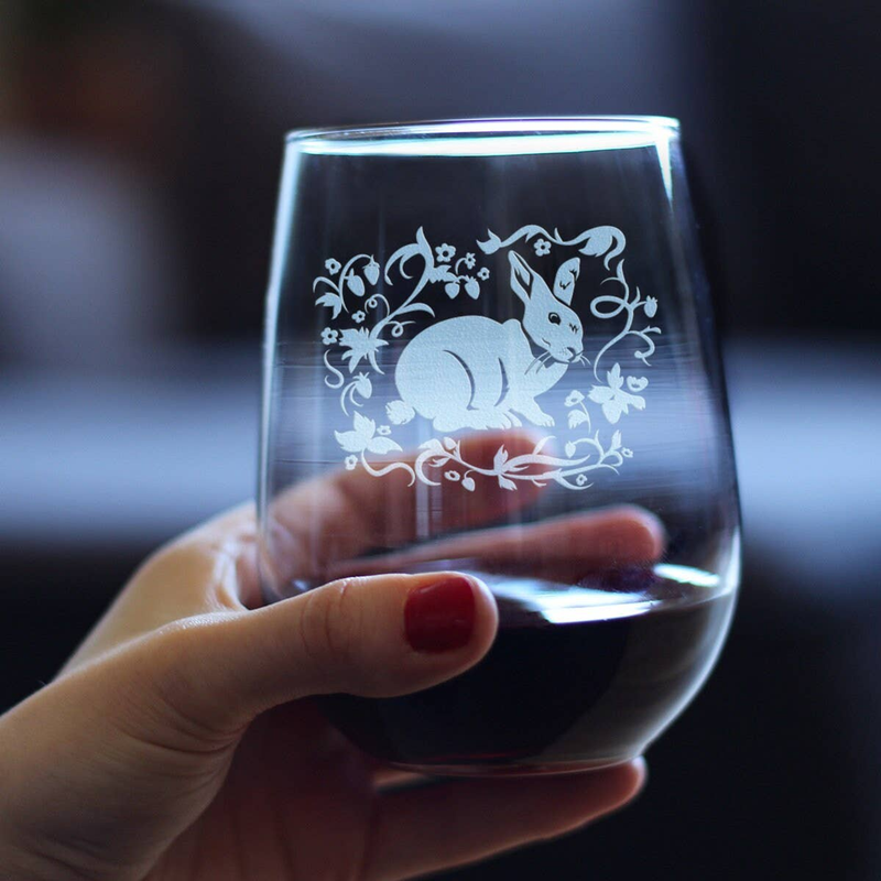 Stemless wine glass with etched rabbit design, held in hand over dark wine