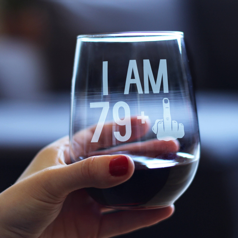 Stemless wine glass held in hand, showing "I AM 79+" etched design with pointing hand