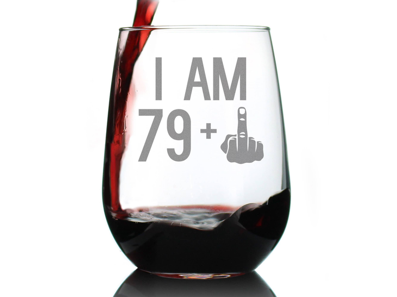 Stemless wine glass with "I AM 79+" etched design, filled with red wine