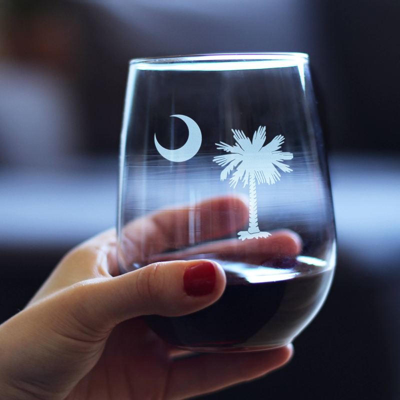 Hand holding a clear stemless wine glass with etched moon and palm tree design.