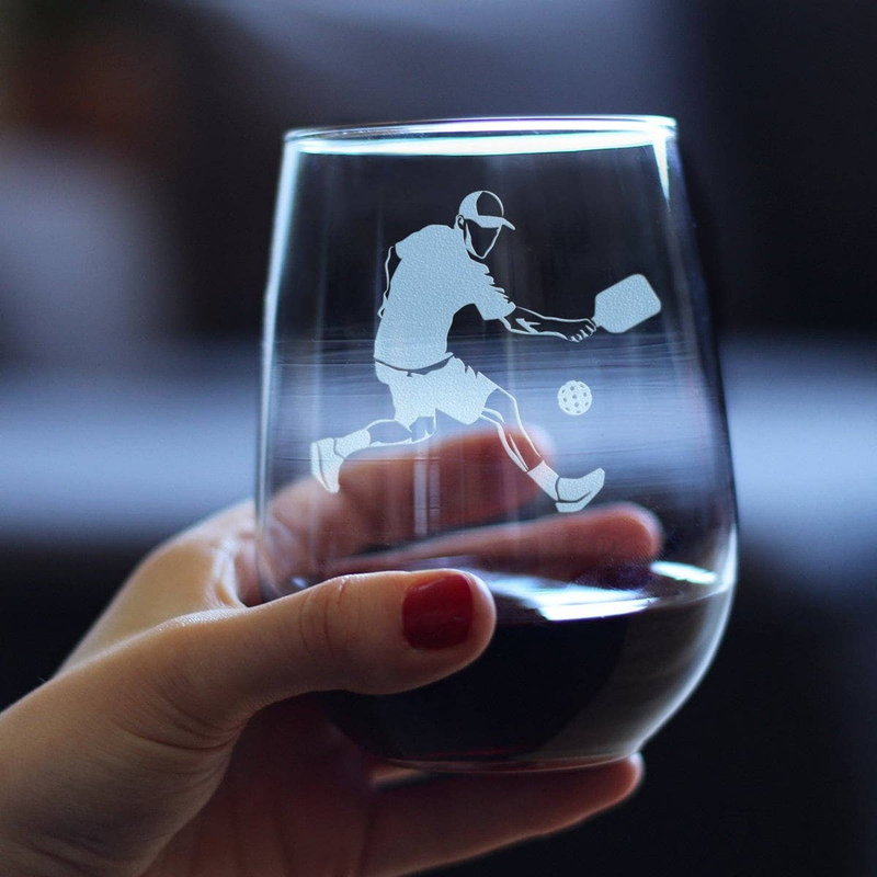 Stemless wine glass held in hand, etched pickleball player on dark red wine