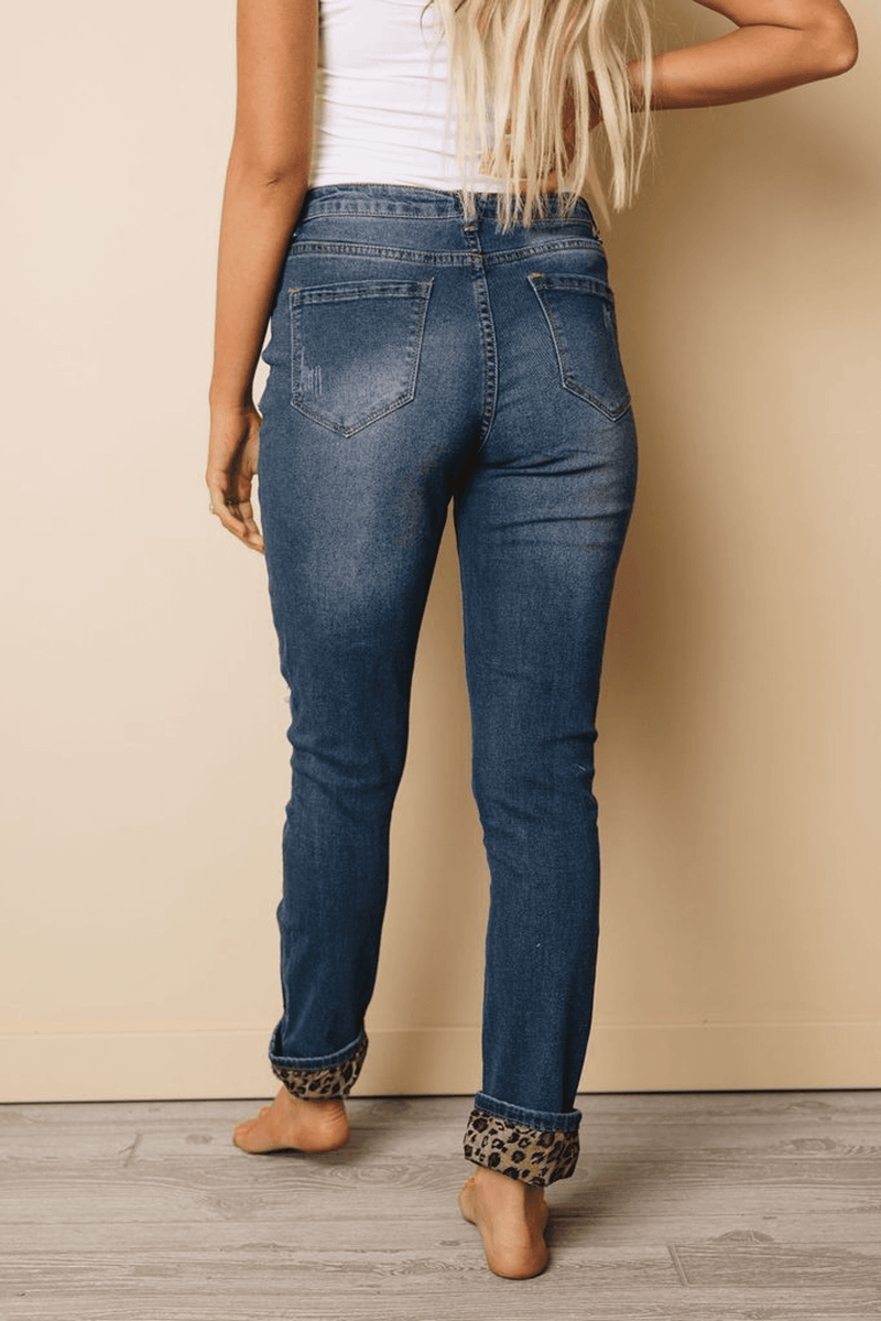 Distressed blue denim jeans with knee rips and leopard-print cuffs at ankles