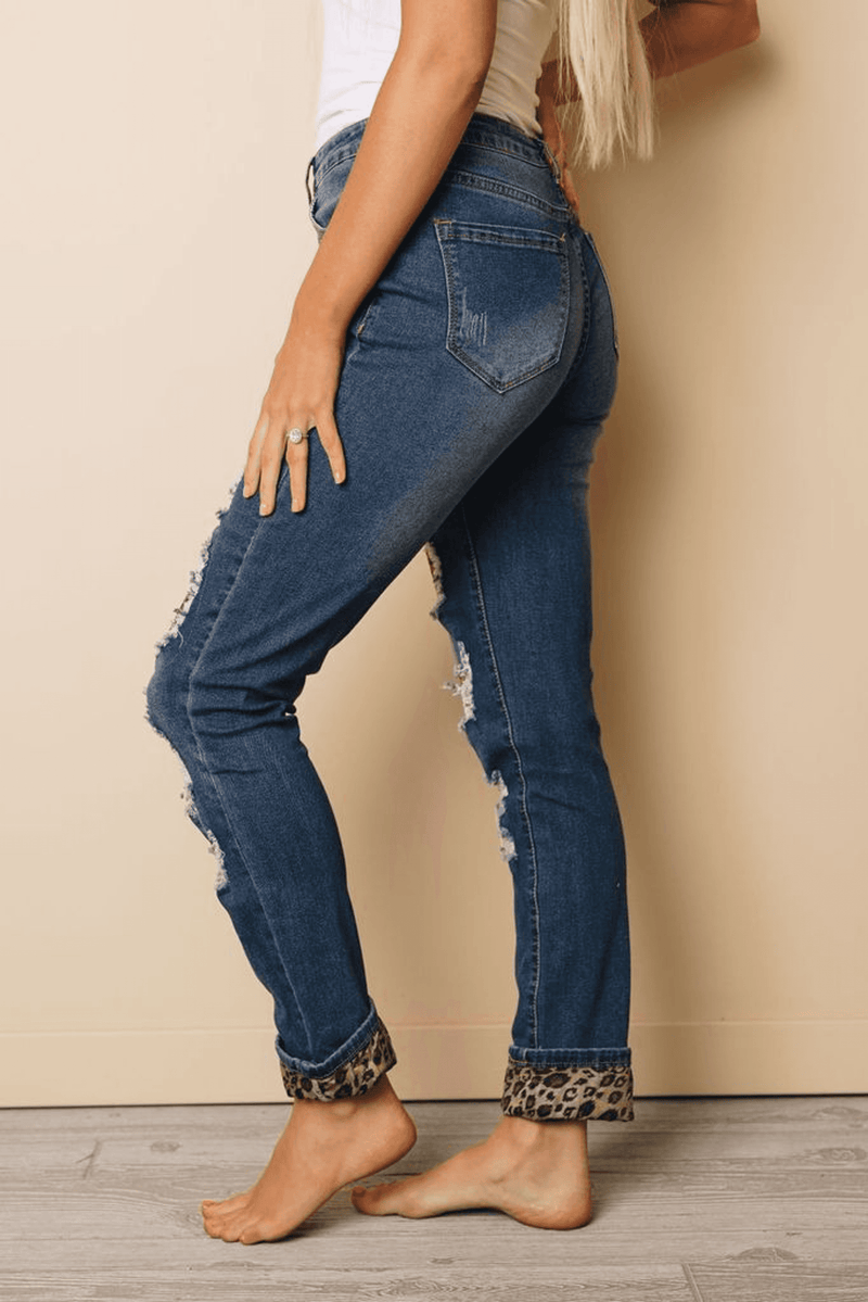 Blue distressed denim jeans with ripped legs and leopard-print cuffs at ankles