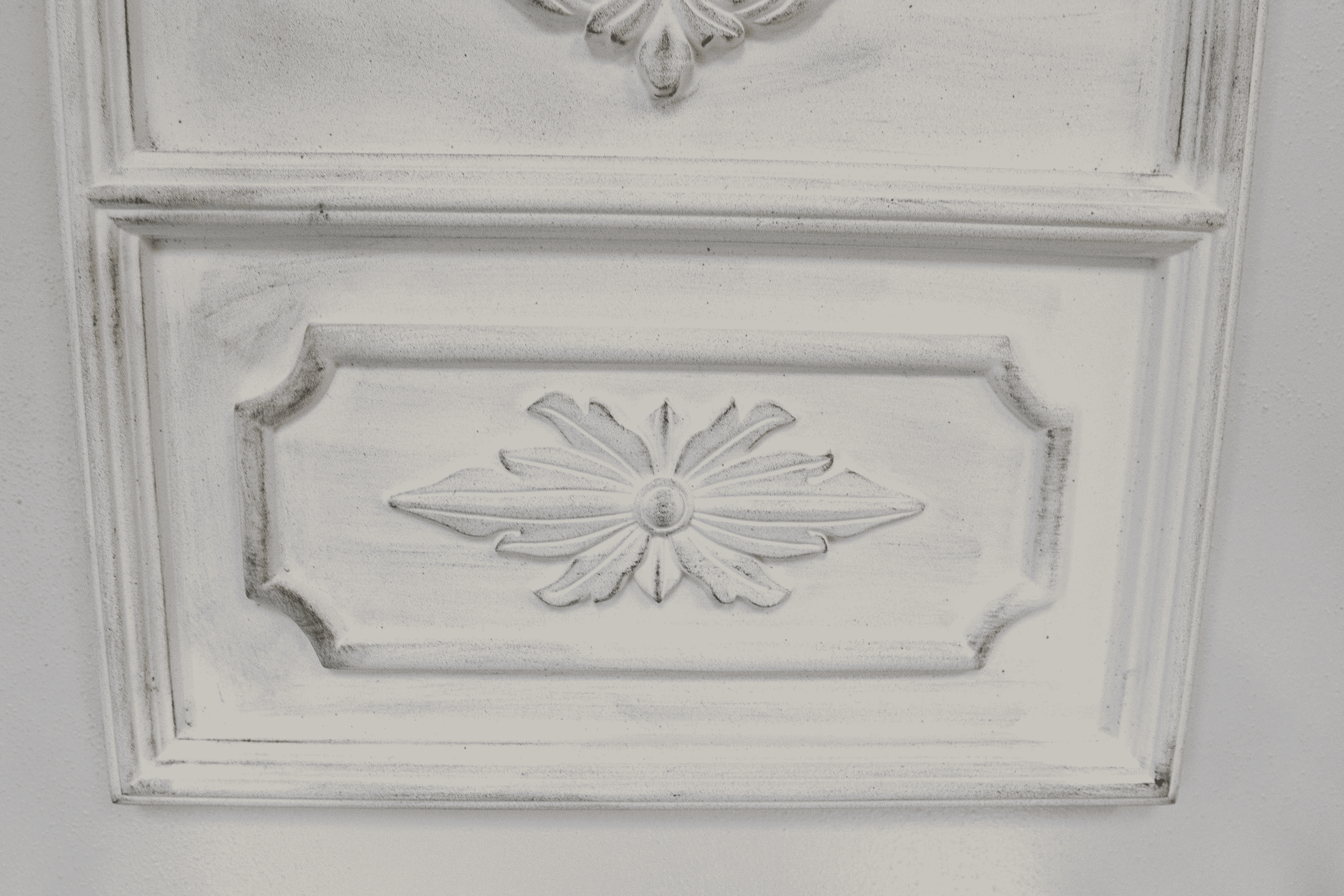 White mirror frame detail with embossed floral medallion on raised rectangular panel
