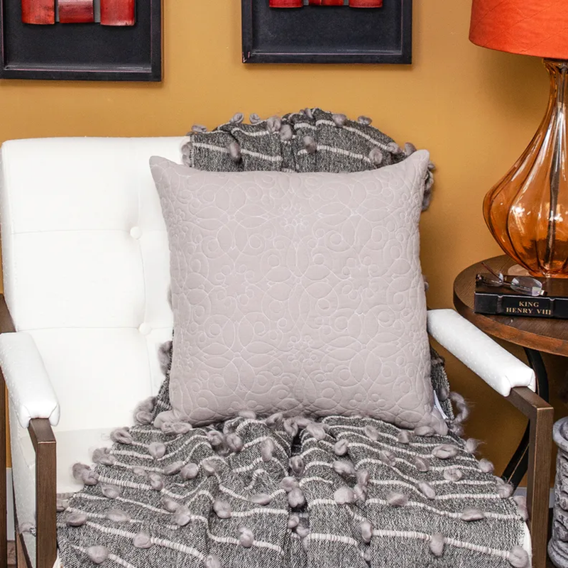 Beige quilted square throw pillow on white seat with textured blanket behind
