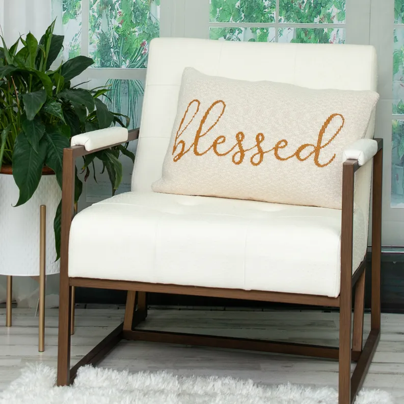 Beige throw pillow with 'Blessed' embroidery on a chair cushion