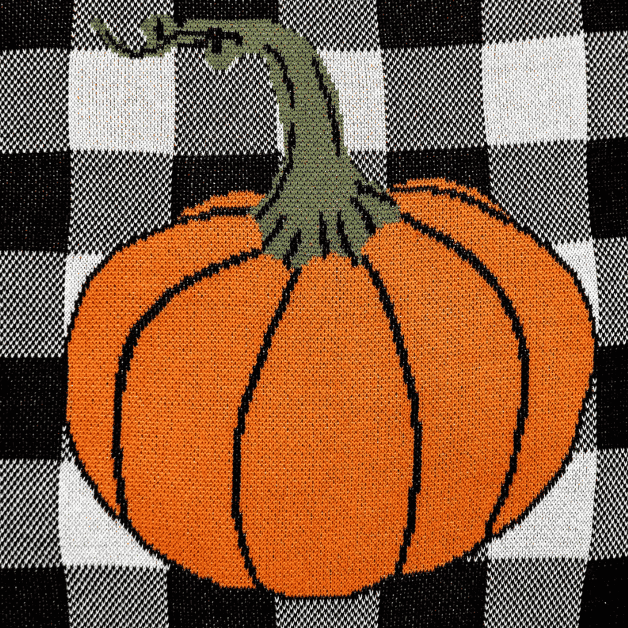 Throw pillow with orange pumpkin and green stem on black-and-white checkered knit.
