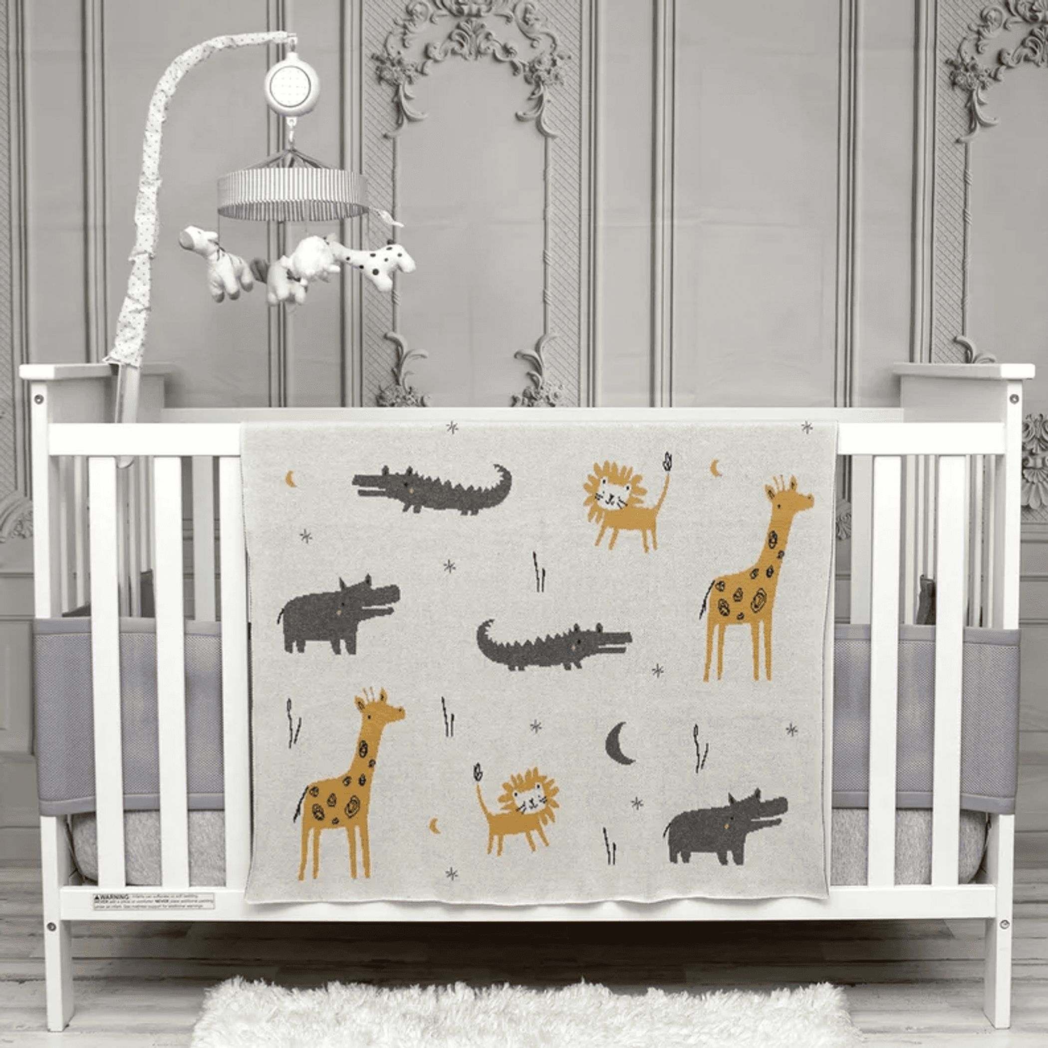 Beige baby blanket with zoo animal pattern, laid across crib rail