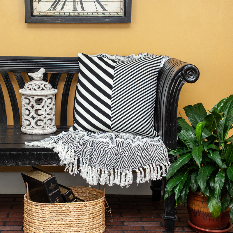 Black and white striped square throw pillow on a bench with fringed throw nearby