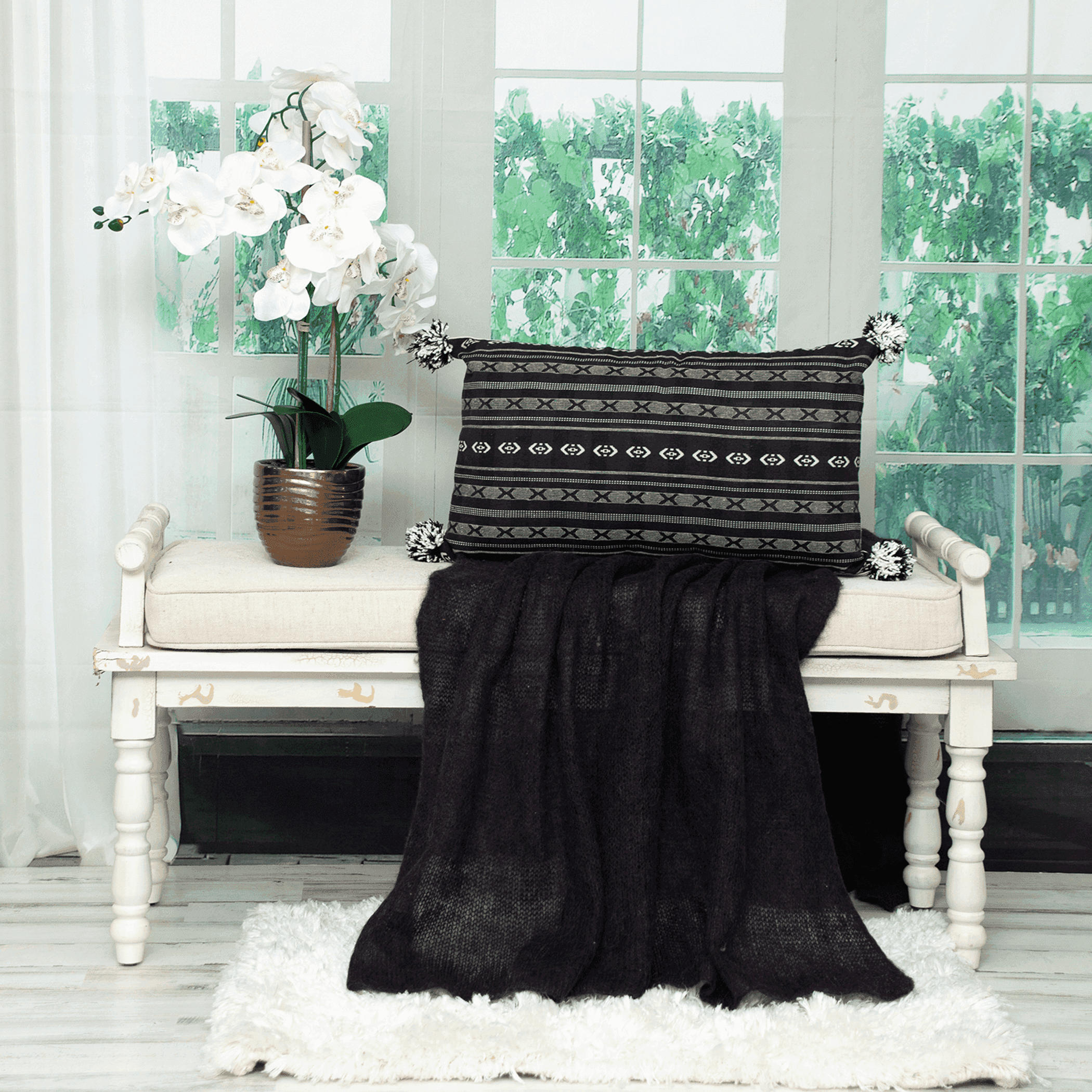 Black transitional throw pillow with layered stripe and X pattern; corner pom accents