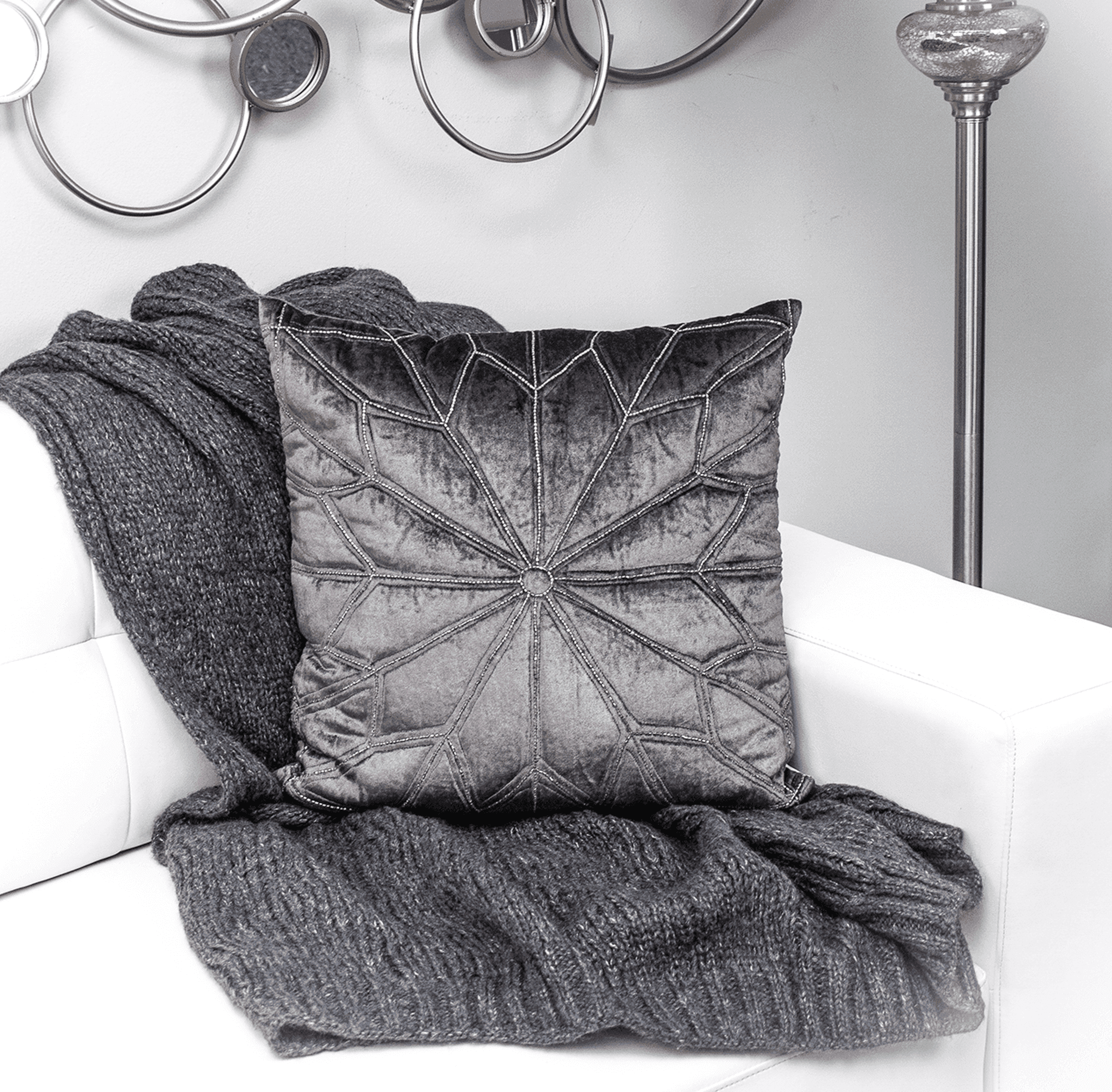Geometric dark gray throw pillow with tufted center detail, placed on a sofa with blanket.