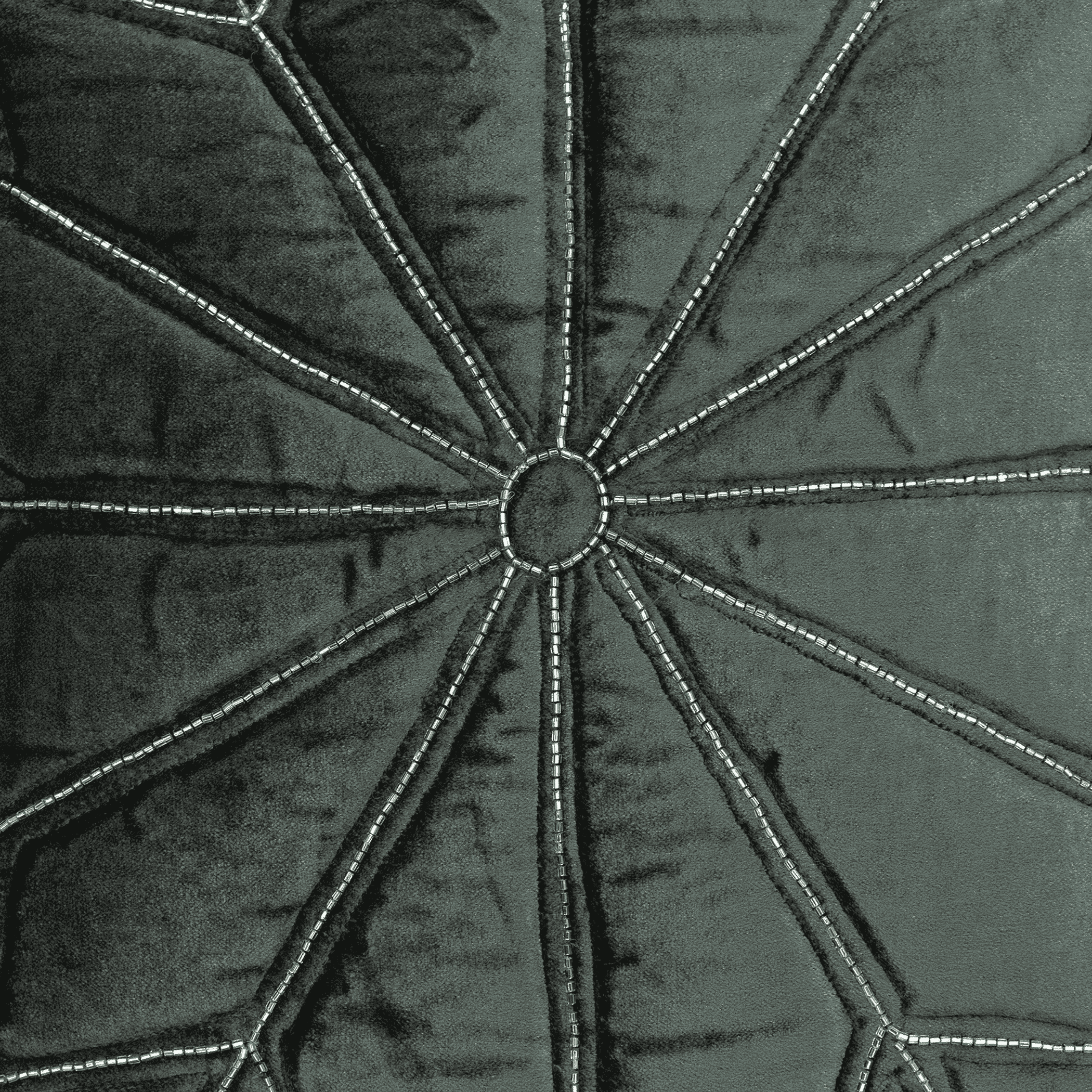 Close-up of dark gray throw pillow: velvet panel with starburst stitching and silver trim.