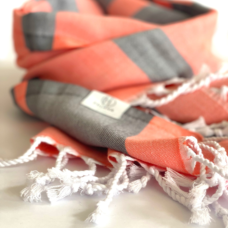 Orange and gray striped Turkish towel with braided white fringe on folded edge