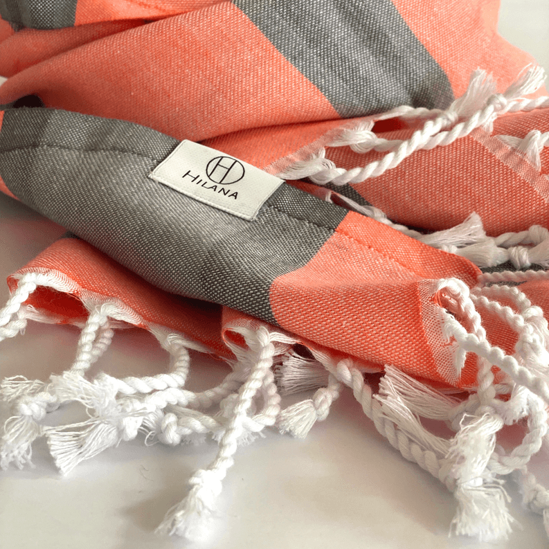 Gray and orange striped Turkish towel detail with white braided fringe and label