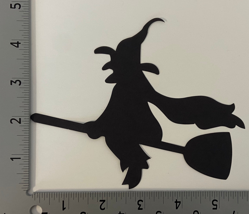 Black witch on broom cut-out silhouette next to a measuring ruler