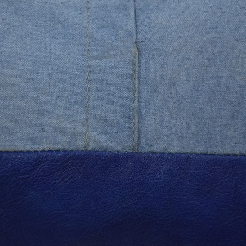 Close-up of blue leather pouf seam where top fabric meets side panel.