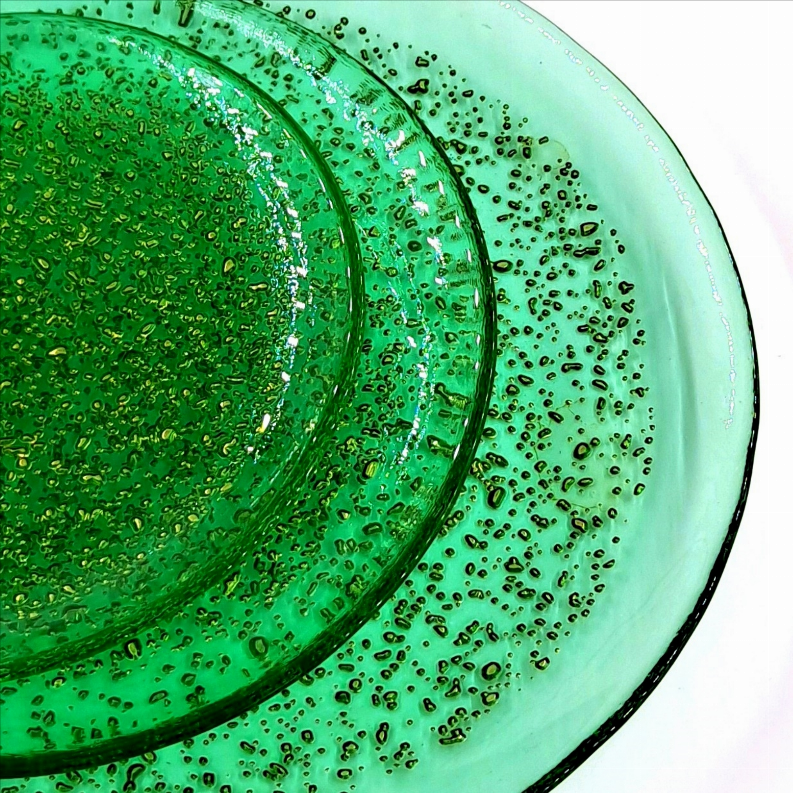 Emerald glass dinner plate with gold speckled glaze, round rim close-up.