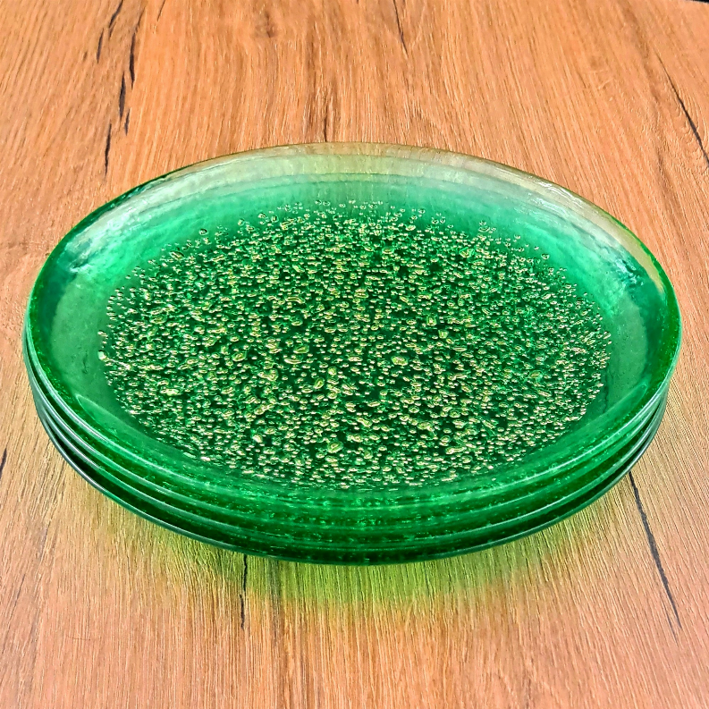 Stacked emerald glass dinner plates with gold speckled finish on wooden surface.