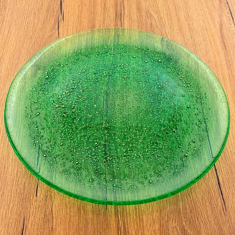 Green emerald glass dinner plate with gold speckles, wide circular rim on wood.