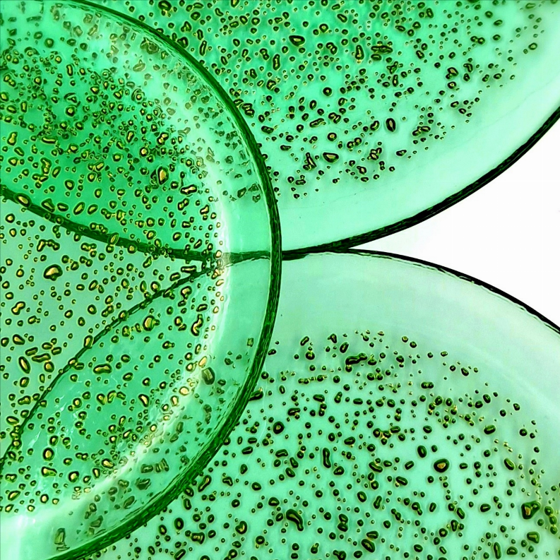 Two emerald glass dinner plates overlapping, gold speckled texture along edges.