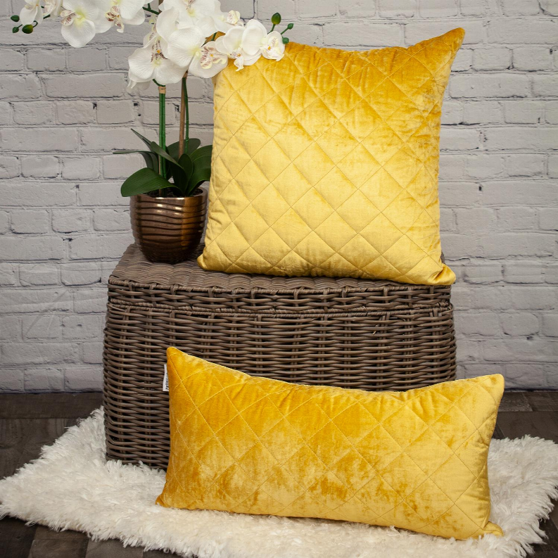 Yellow quilted throw pillow with diamond stitch pattern on a textured surface