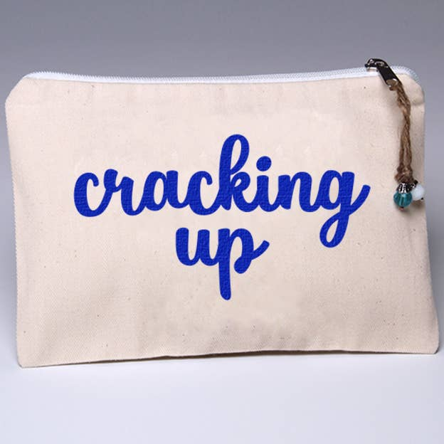 Cream canvas zip pouch with blue 'cracking up' text and braided zipper pull