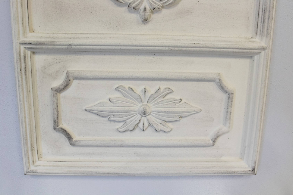 White mirror frame close-up with embossed floral rosette on raised rectangular panel