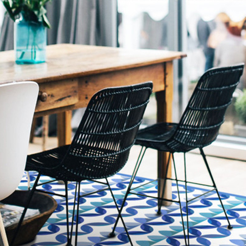 Blue-and-white vinyl floor mat with repeating leaf-and-flower pattern under black patio chairs