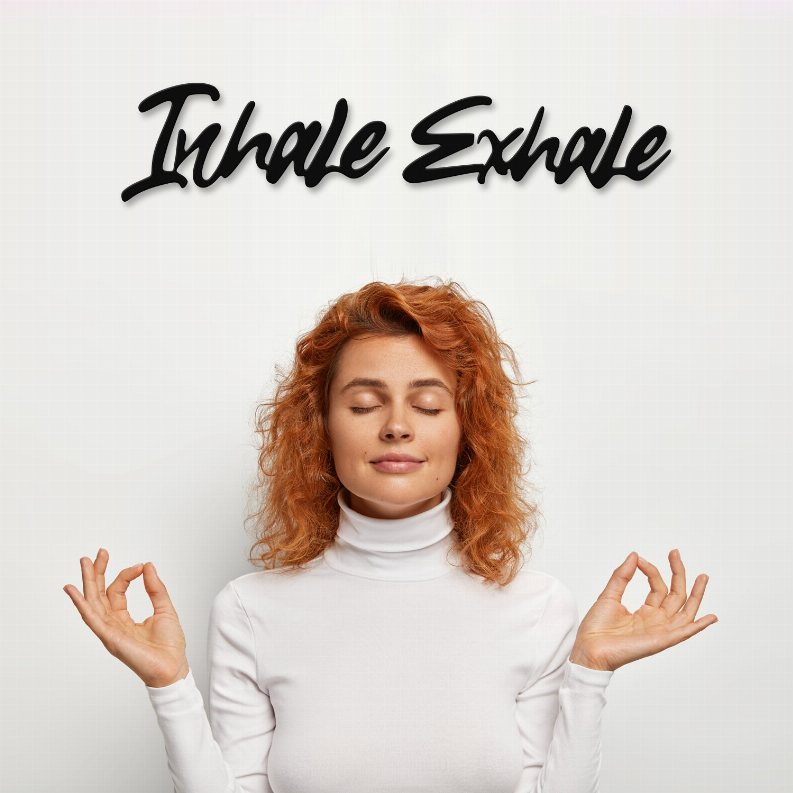 Metal wall art with black “Inhale Exhale” script lettering on a plain wall.