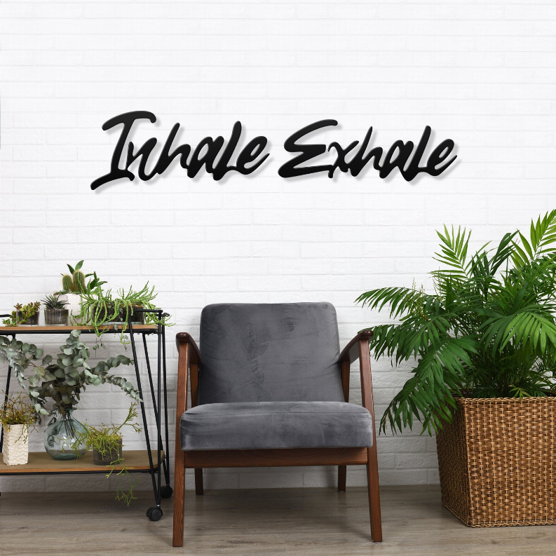 Metal wall art sign with “Inhale Exhale” in black script on a white brick wall.