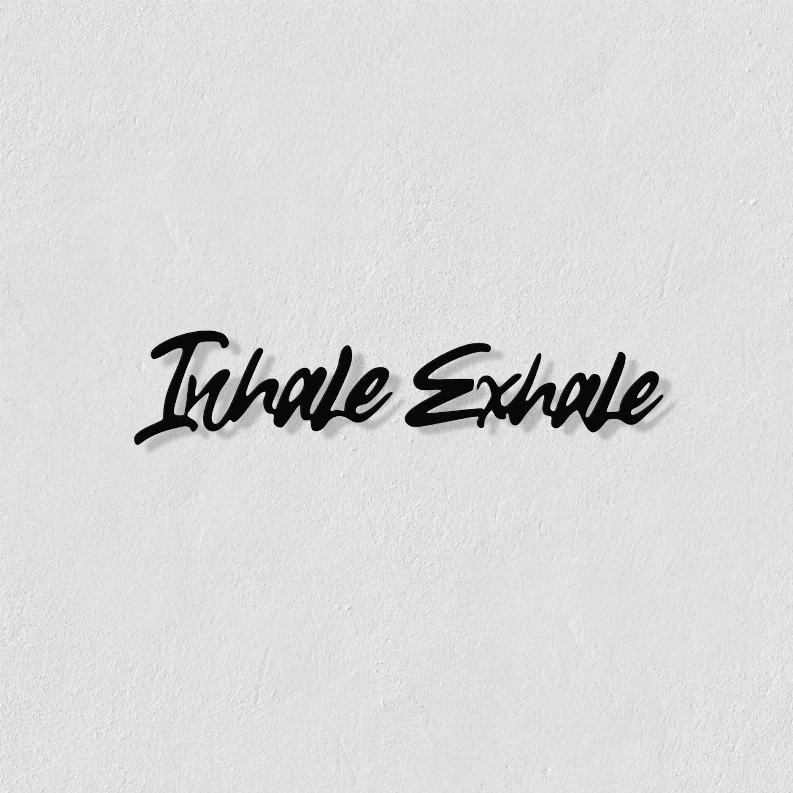 Metal wall art close-up: black “Inhale Exhale” script on white textured wall.