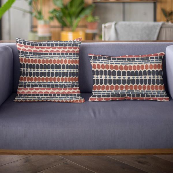 Red and blue brick-pattern throw pillow with striped border on a gray sofa.