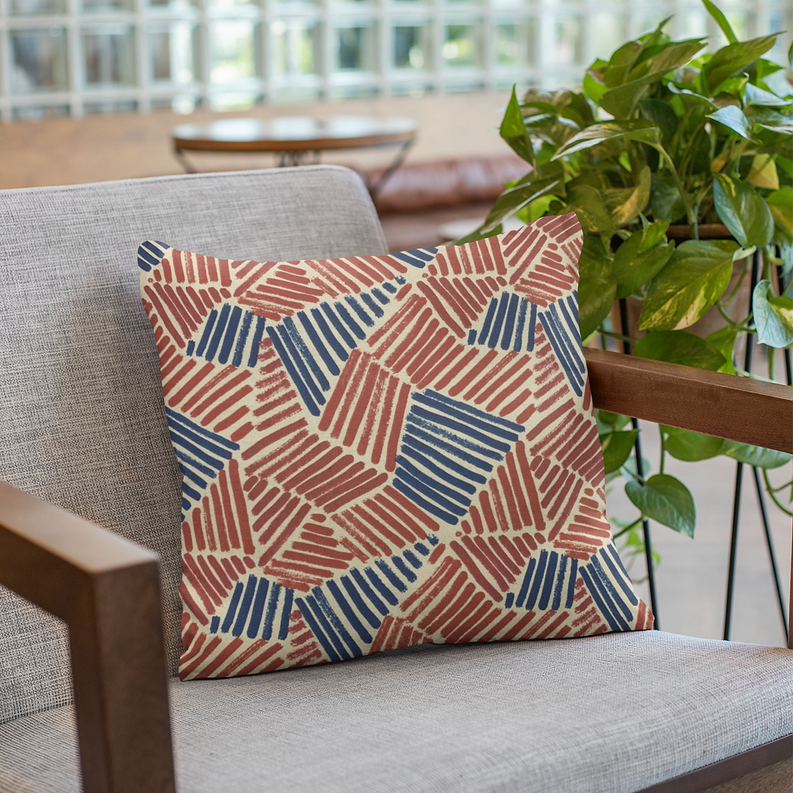 Square throw pillow with red and blue abstract geometric stripe pattern on light fabric.
